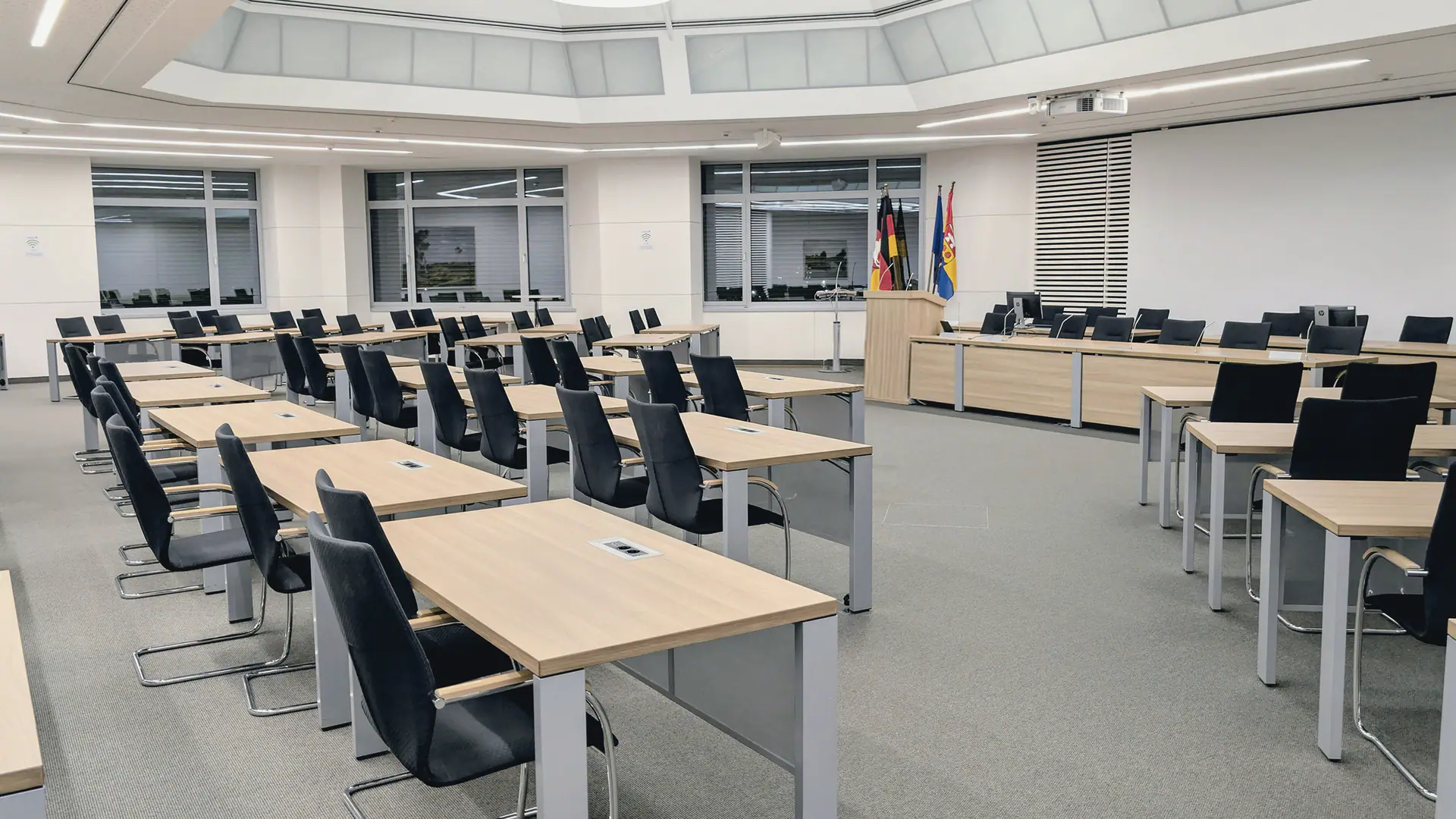Leerer Plenarsaal mit Tischreihen und Flaggen